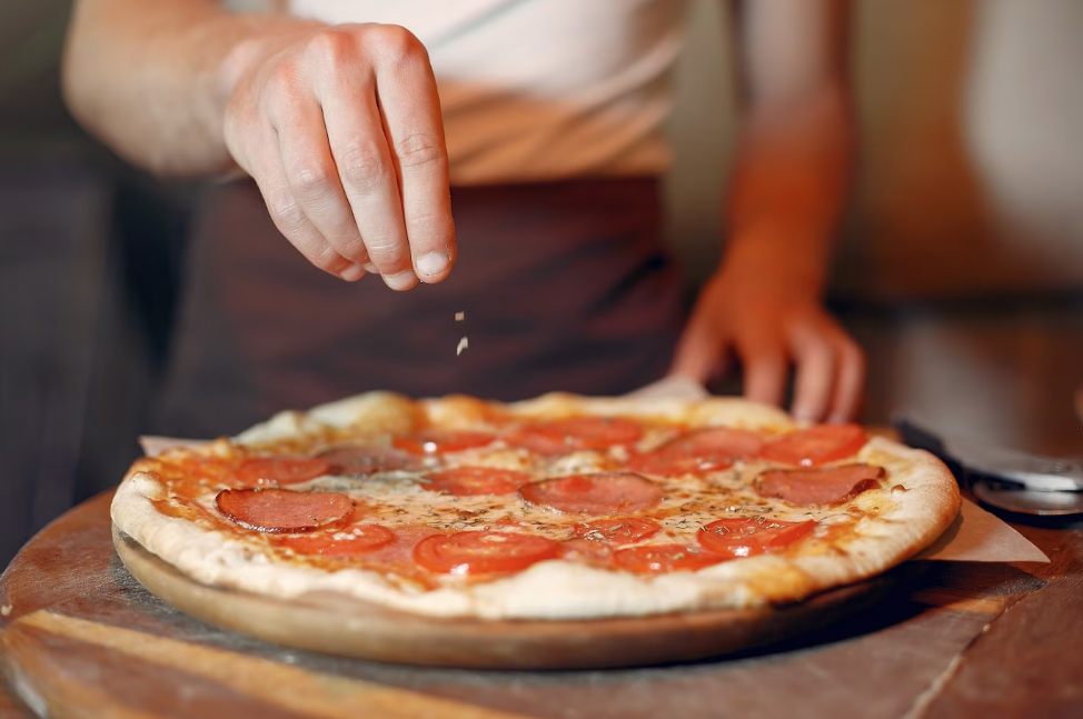 Foto de una persona poniendole especias a una pizza